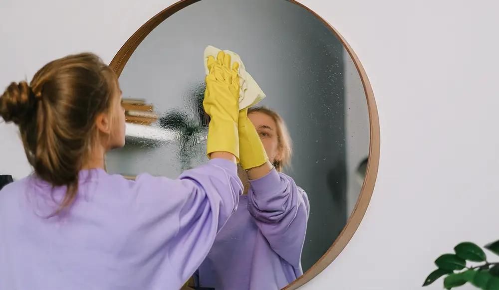 Woman cleaning a big mirror with yellow cleaning gloves