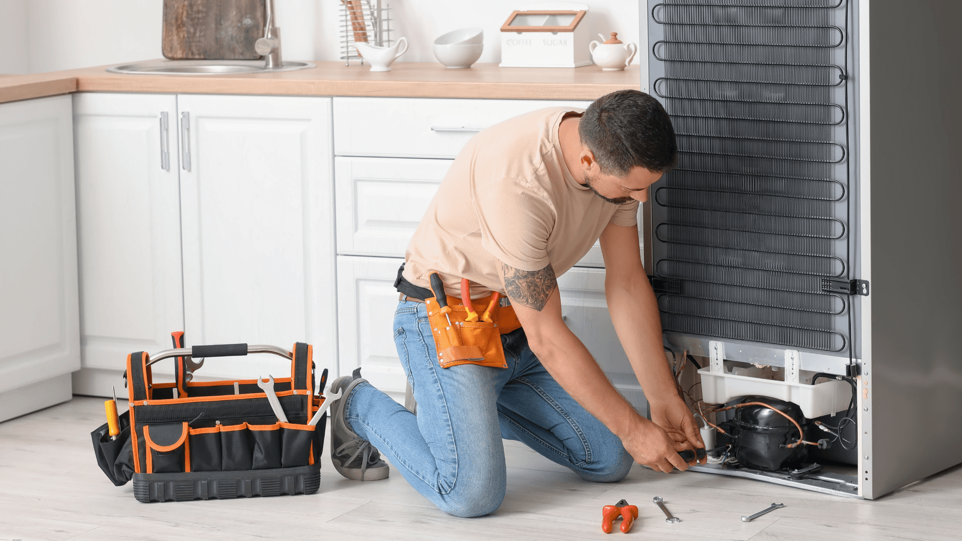 Man on his knees with tools fixing the back of a refrigerator 
