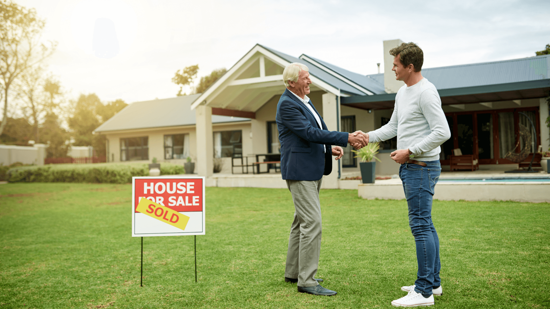 Two men shaking hands in front of a for sale sign for a house on the market