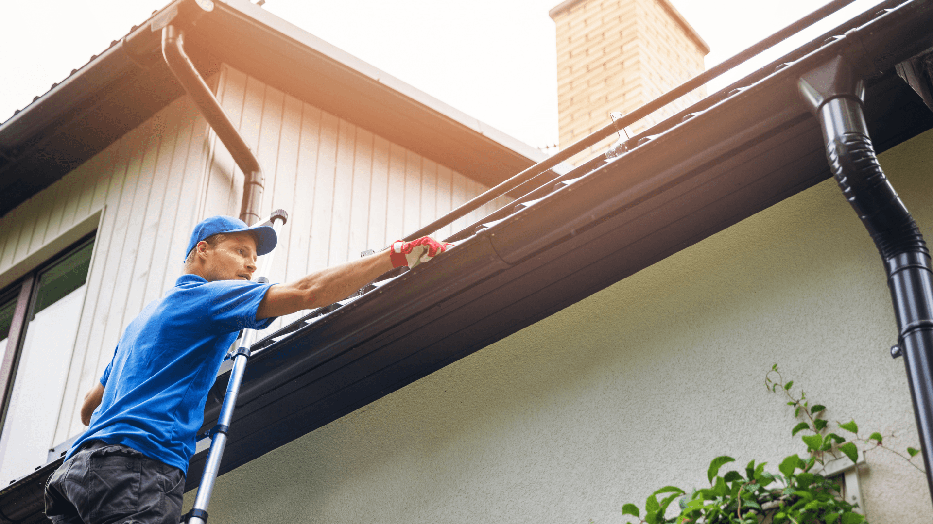 Man standing on a ladder cleaning the gutters on his roof 