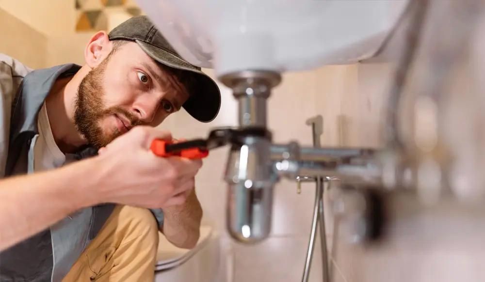 Plumber fixing sink pipes with wrench