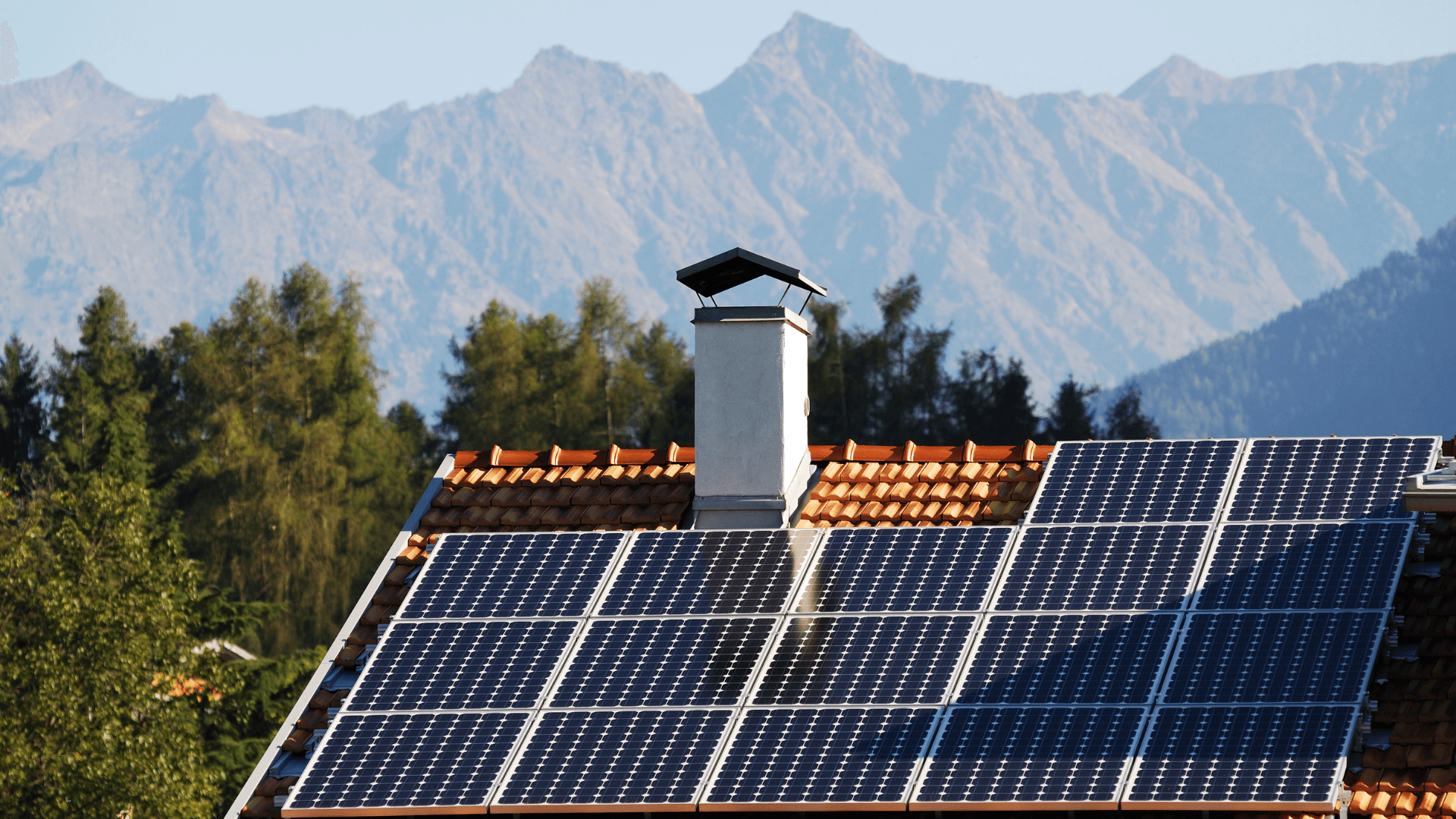 Several solar panels on a house with mountains in the background 
